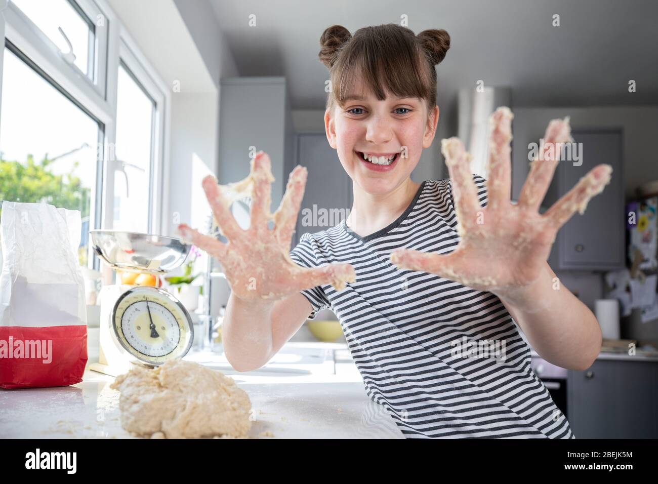Portrait Of Girl With Messy Hands Having Fun In Kitchen Kneading Dough For Baking Stock Photo