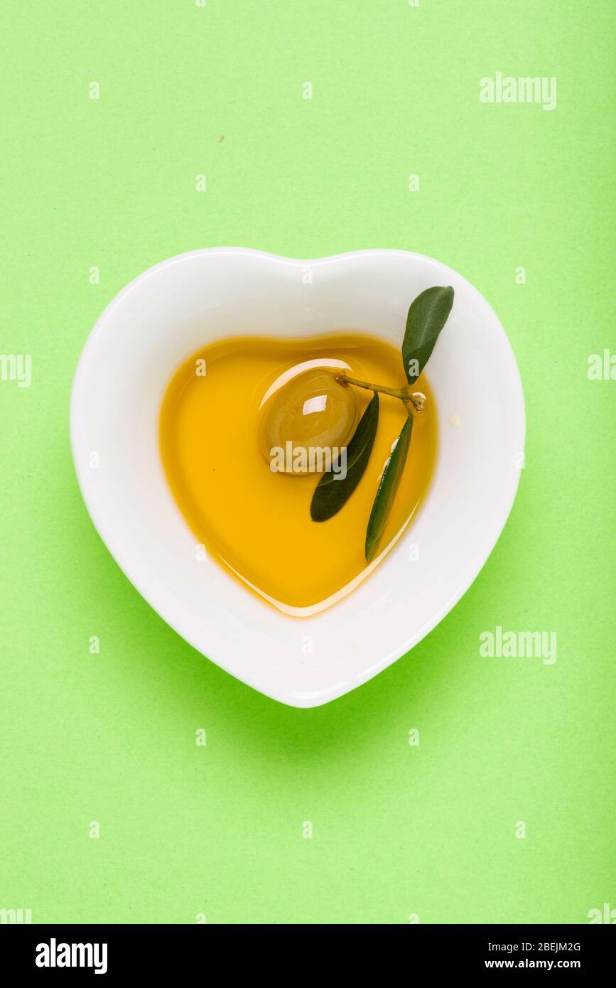 seen from above, an olive immersed in a heart-shaped bowl with extra virgin olive oil. Green uniform background. still life Stock Photo