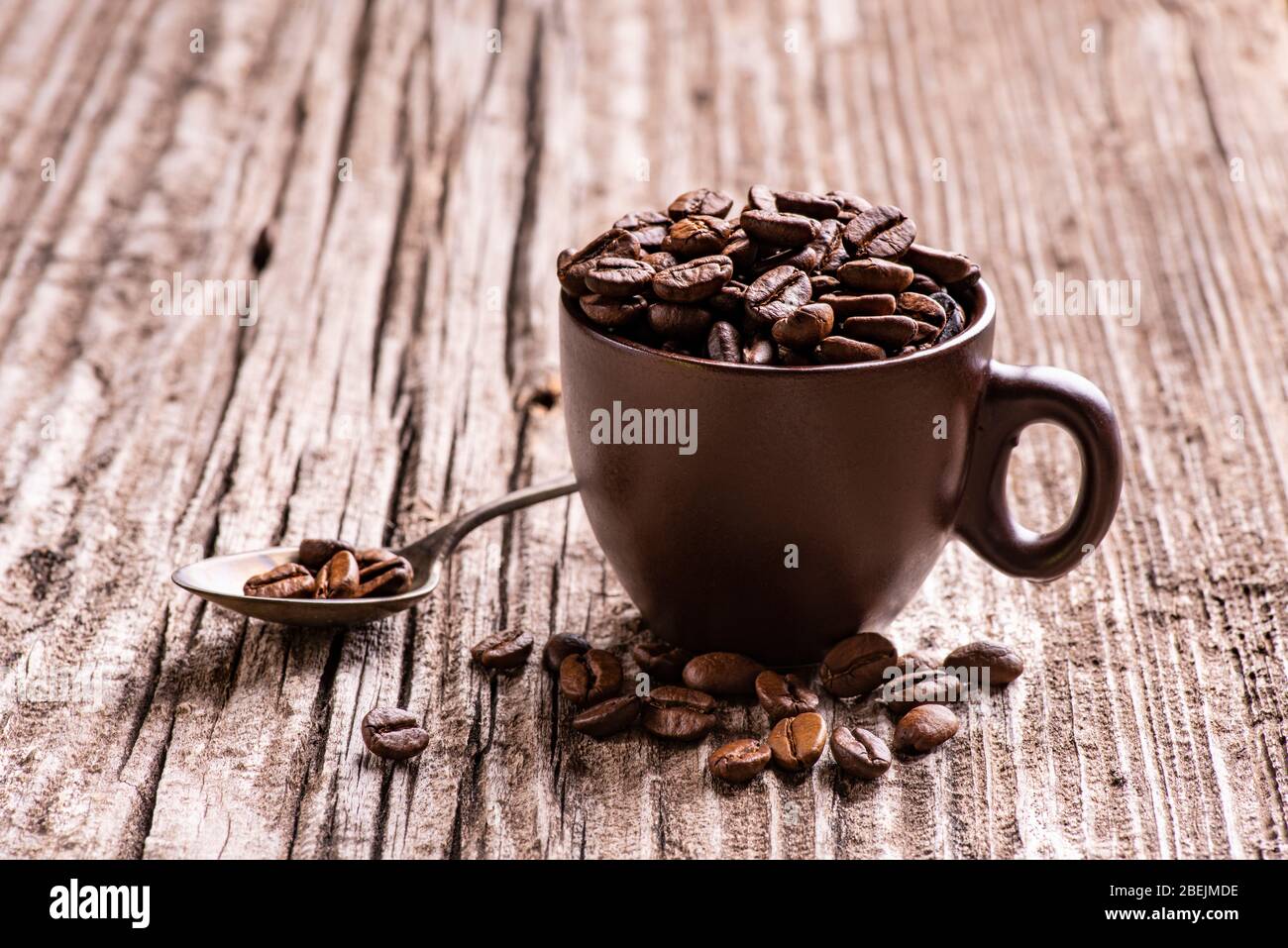 in the foreground, on worn wood, roasted coffee beans in the brown ceramic cup. Stock Photo