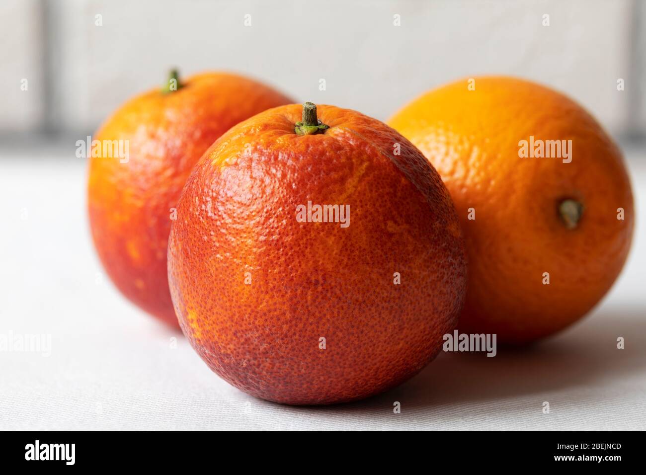 Three Sicilian blood red oranges isolated laying on the tablecloth on white brick wall background Stock Photo