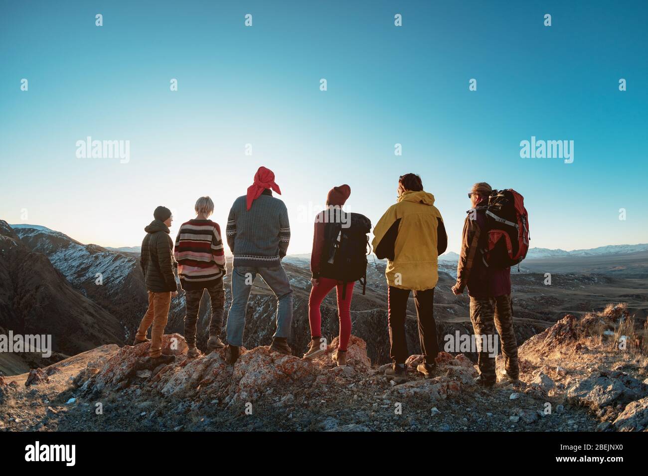Group of hikers are standing on mountain top and looking at sunset Stock Photo