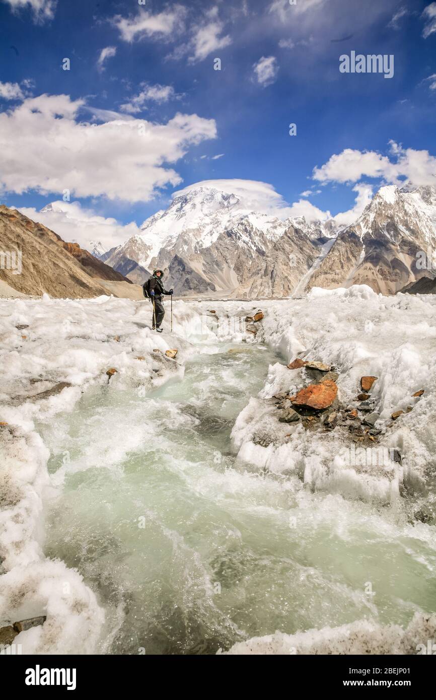 A sigle, solitary hiker, trekker, walker by a stream on the Vigne Glacier in the Karakoram Mountains in Northern Pakistan. Broad Peak in the distance. Stock Photo