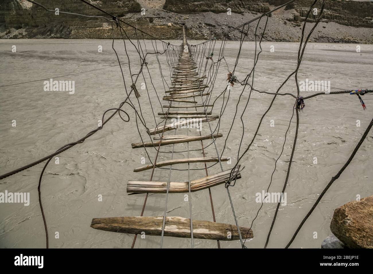 A very dangerous suspension type footbridge crossing the Hunza River near Passu, in Northern Pakistan. Stock Photo