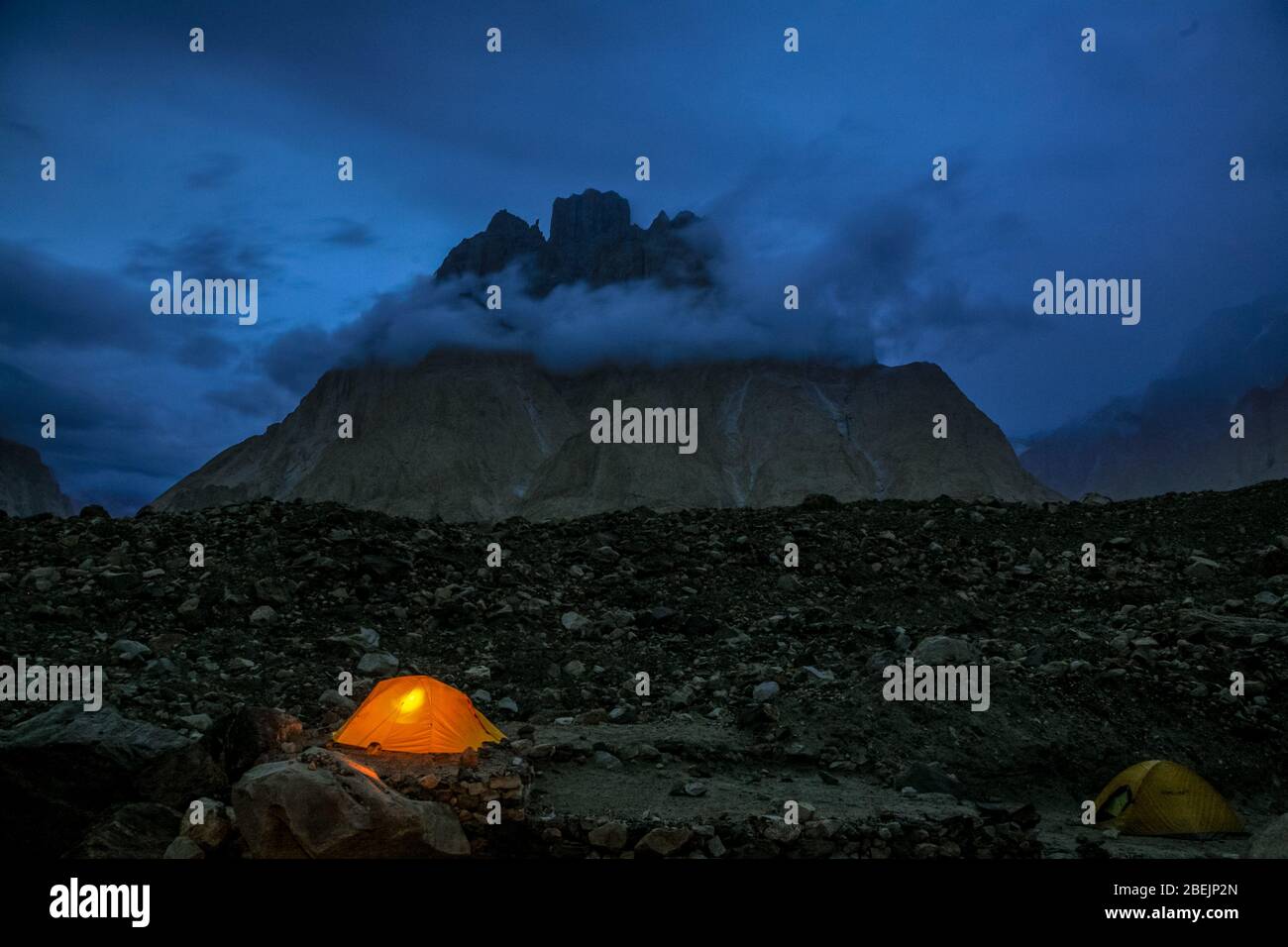 A small tent, lit from the inside, during late evening in front of Trango Tower on the Baltoro Glacier in the Karakoram Mountains in Pakistan. Stock Photo