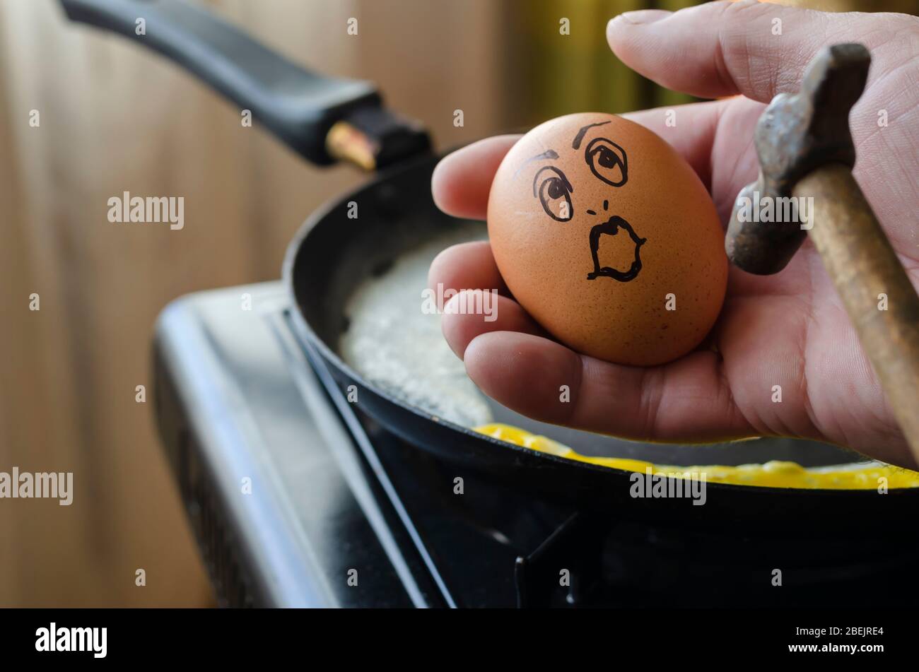 Surprised chicken egg in hand in front of a hammer. Raw chicken egg