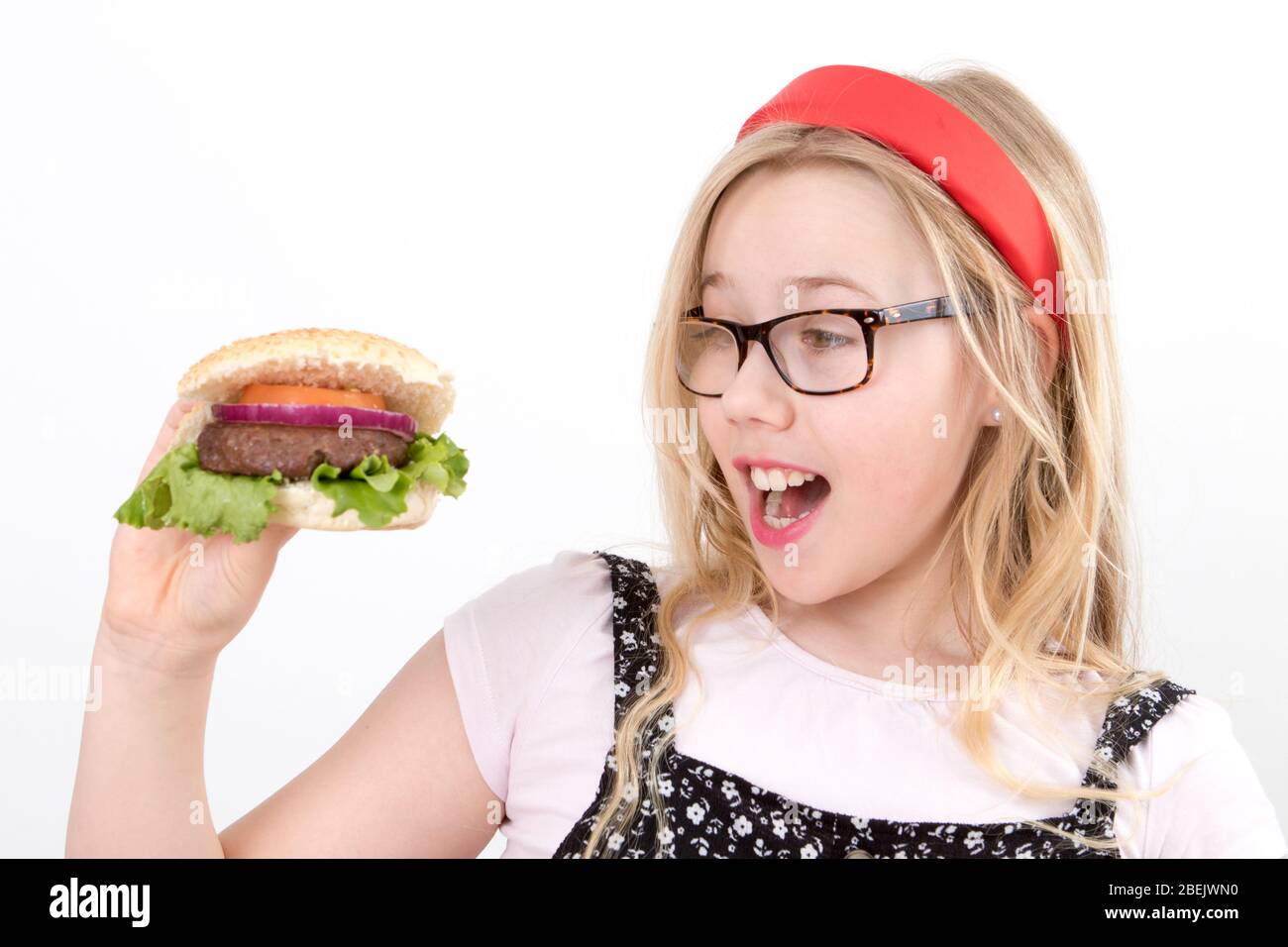 Young blonde girl wearing glasses in a red Alice band holding a homemade burger Stock Photo
