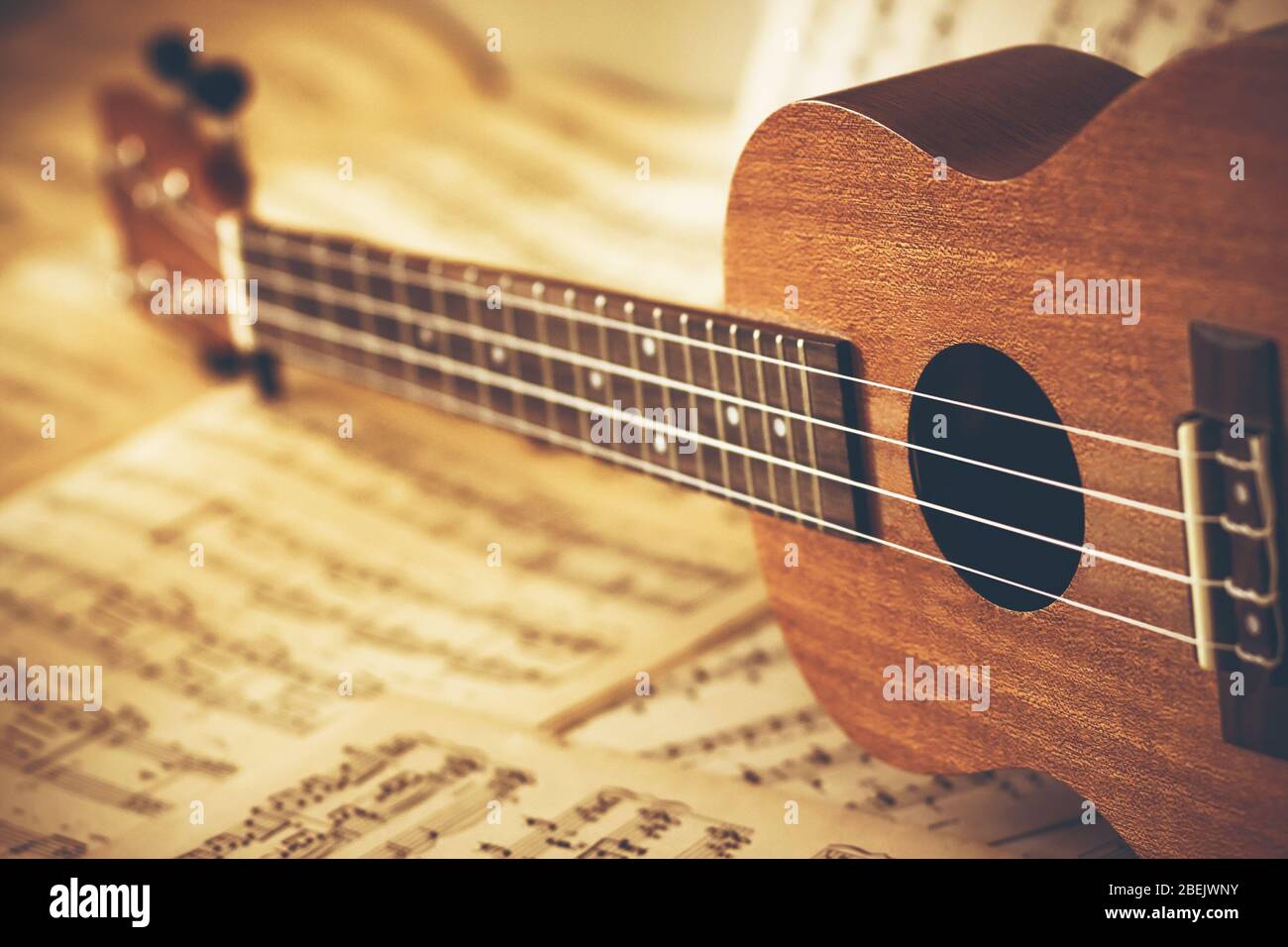 An ukulele with nylon strings lies on its side on scattered sheets of paper with notes on it. Music lessons and learning solfeggio. Stock Photo