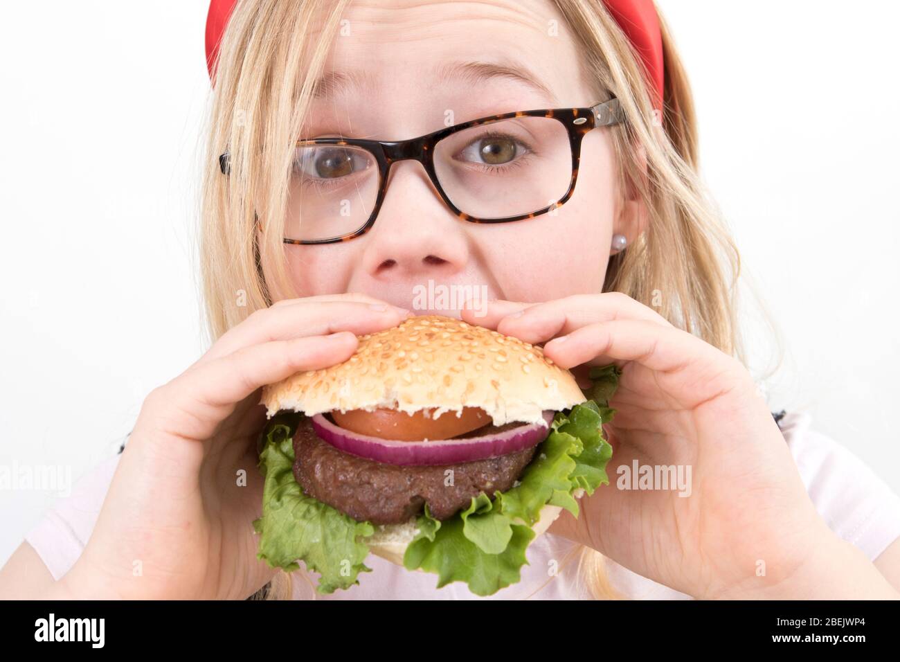 Young blonde girl wearing glasses in a red Alice band eating a homemade burger Stock Photo