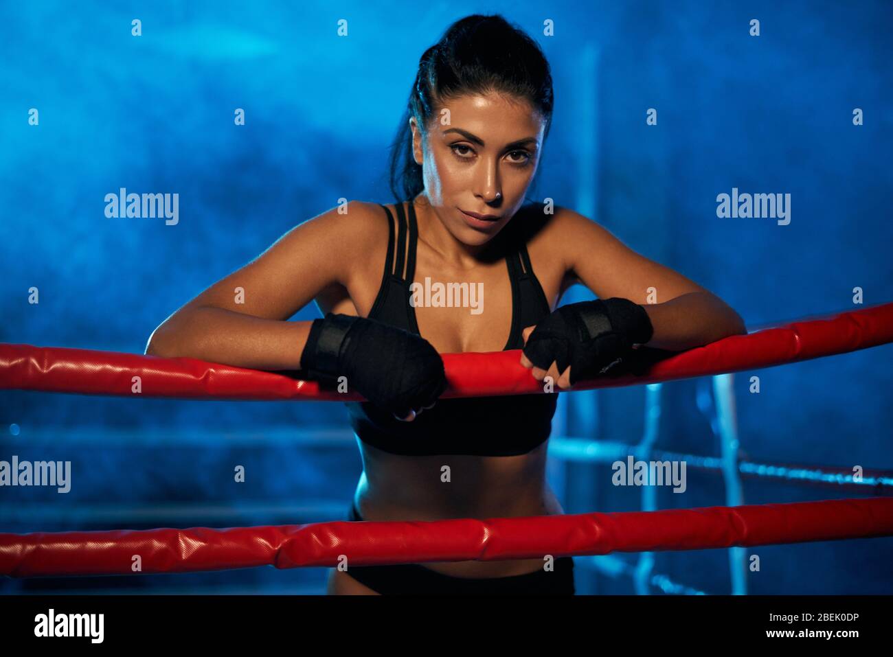 Professional female kickboxer with strong face posing in smoky blue