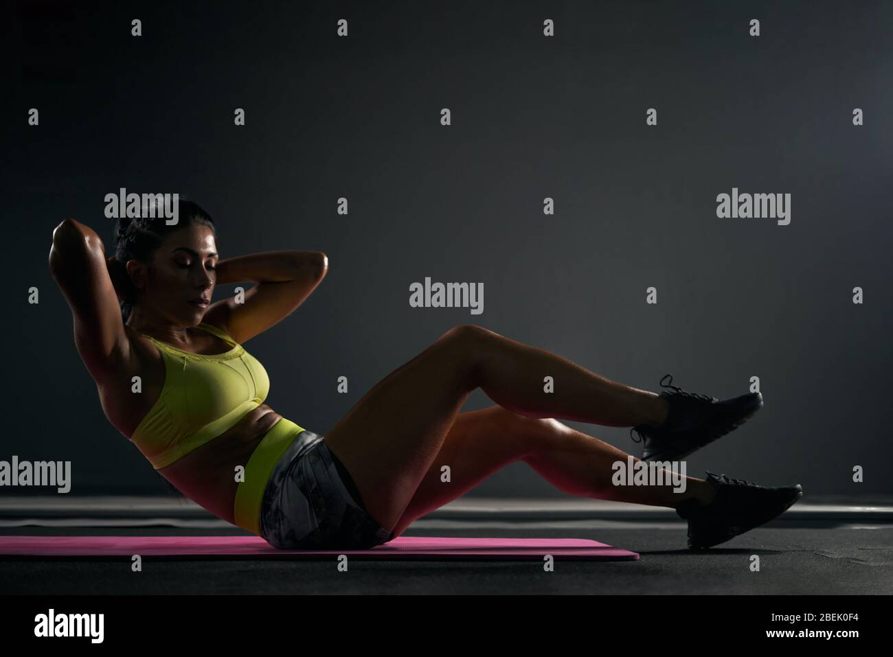 Side view of fit muscular female bodybuilder in bright sportswear doing  crunches in gym. Fit woman with black hair training abs on pink mat in dark  at Stock Photo - Alamy