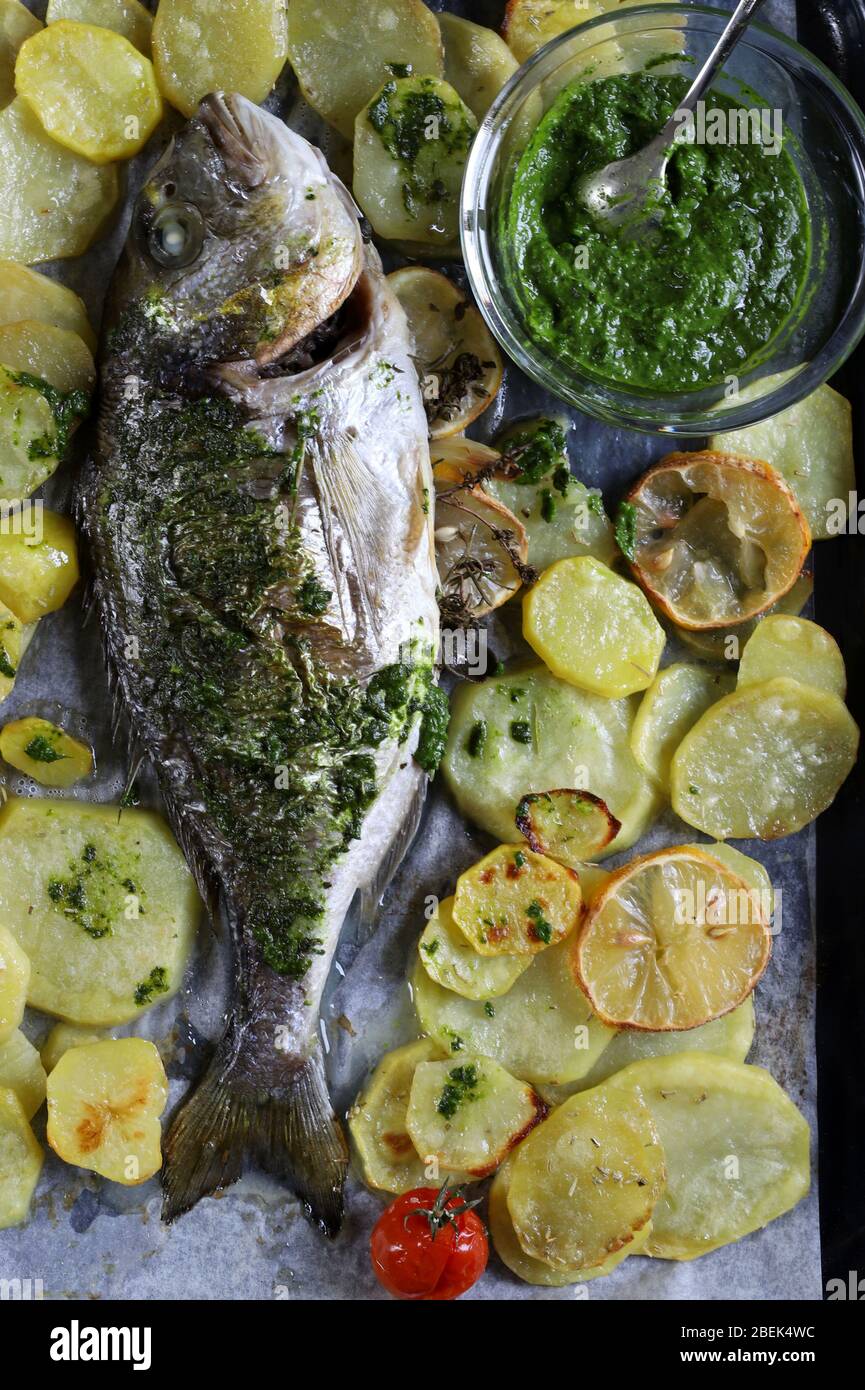 Concept of  homemade healthy food. Baked sea bream with potatoes and green sauce. Directly above. Stock Photo
