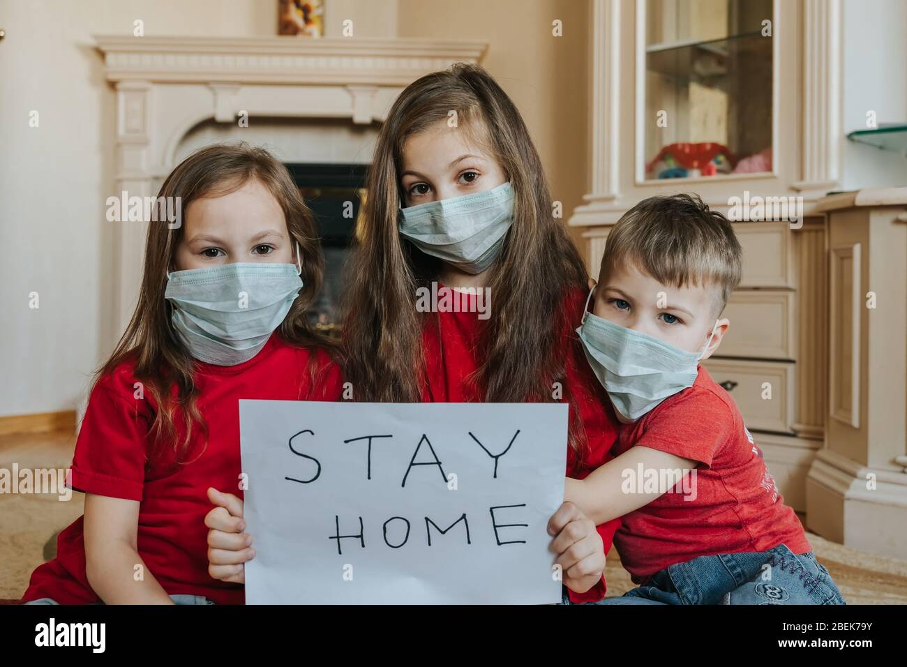 Family stay at home concept. Three children in mask holding sign saying stay at home for virus protection and take care of their health from COVID-19 Stock Photo