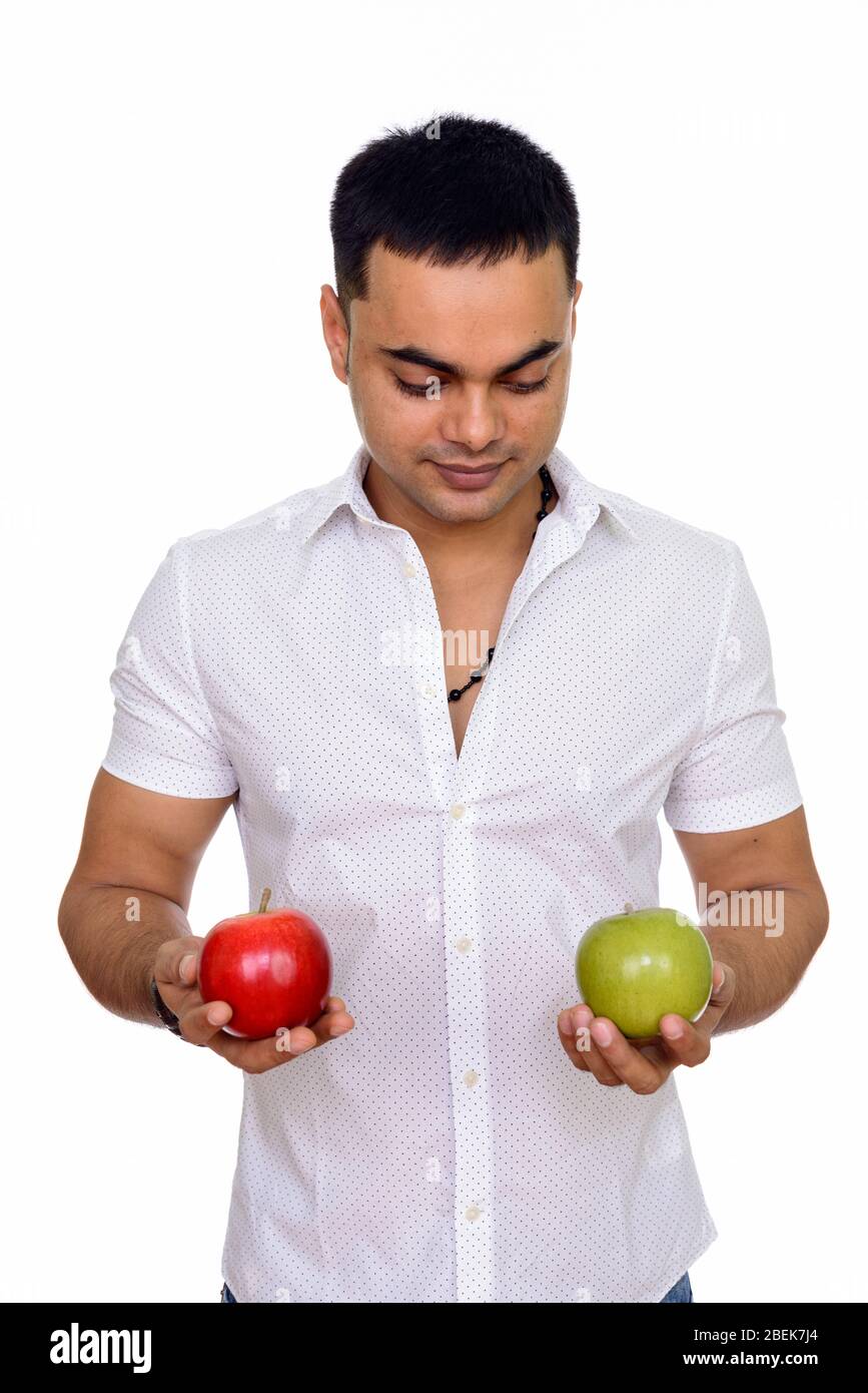 Studio shot of young handsome Indian man holding red and green apple ...