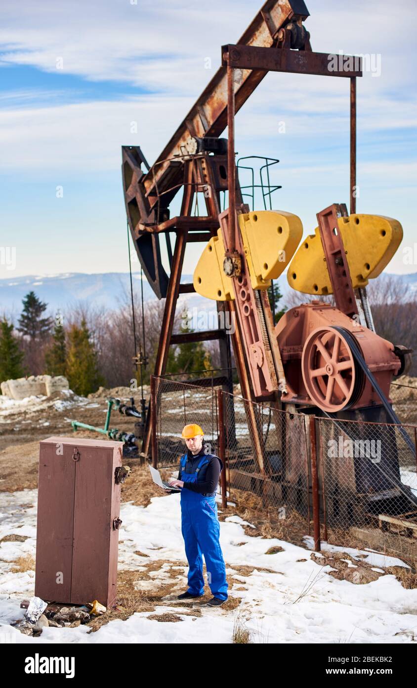 Petroleum engineer in work overalls and helmet using laptop at oil