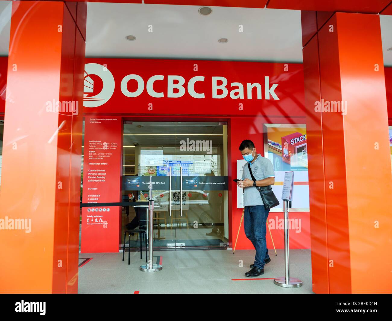 SINGAPORE – 9 APR 2020 – Man wearing face mask outside the entrance of an OCBC Bank branch. The OCBC logo is clearly visible. Stock Photo