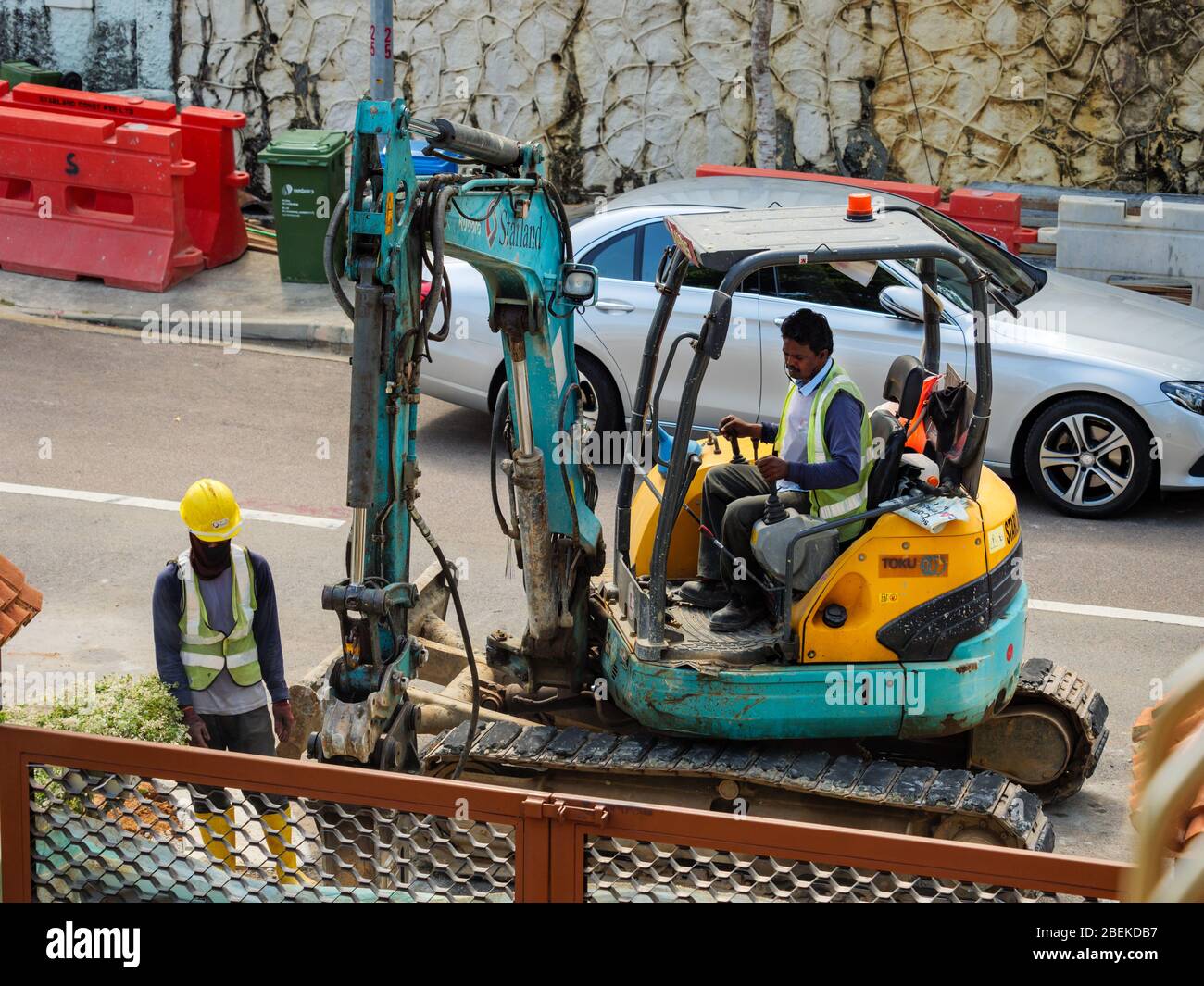SINGAPORE – 28 FEB 2020 - Indian / Bangladeshi  construction workers use a digger to perform road works at a residential estate in Singapore Stock Photo