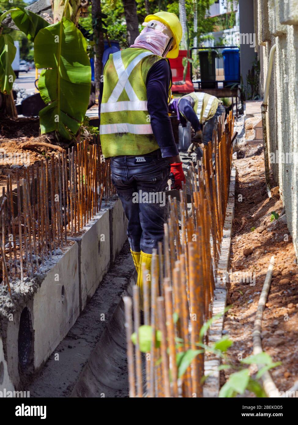 SINGAPORE – 3 MAR 2020 – Construction workers in high visibility protective gear working on a drain at a road works site in Singapore Stock Photo