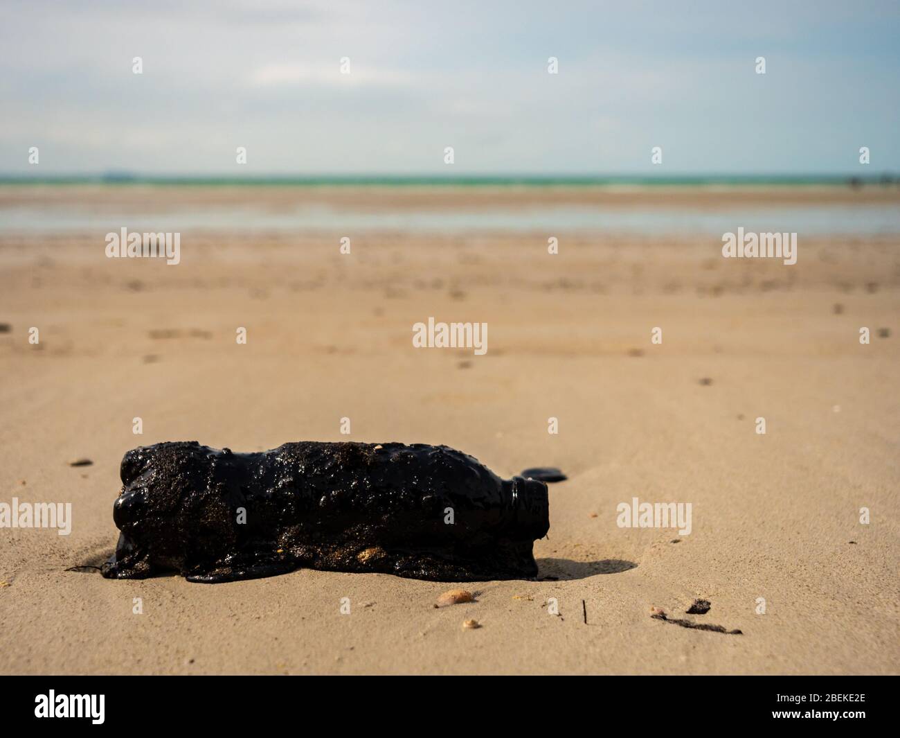BINTAN, INDONESIA – 7 MAR 2020 – Plastic bottle covered in tar and oil sludge from marine oil spills on Lagoi Beach Stock Photo