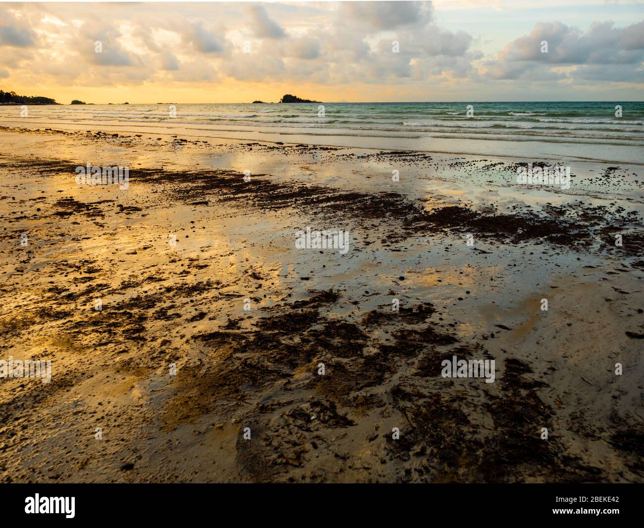 BINTAN, INDONESIA – 7 MAR 2020 – Tar balls and oil sludge from marine oil spills wash up on Lagoi beach during a beautiful sunset causing pollution Stock Photo