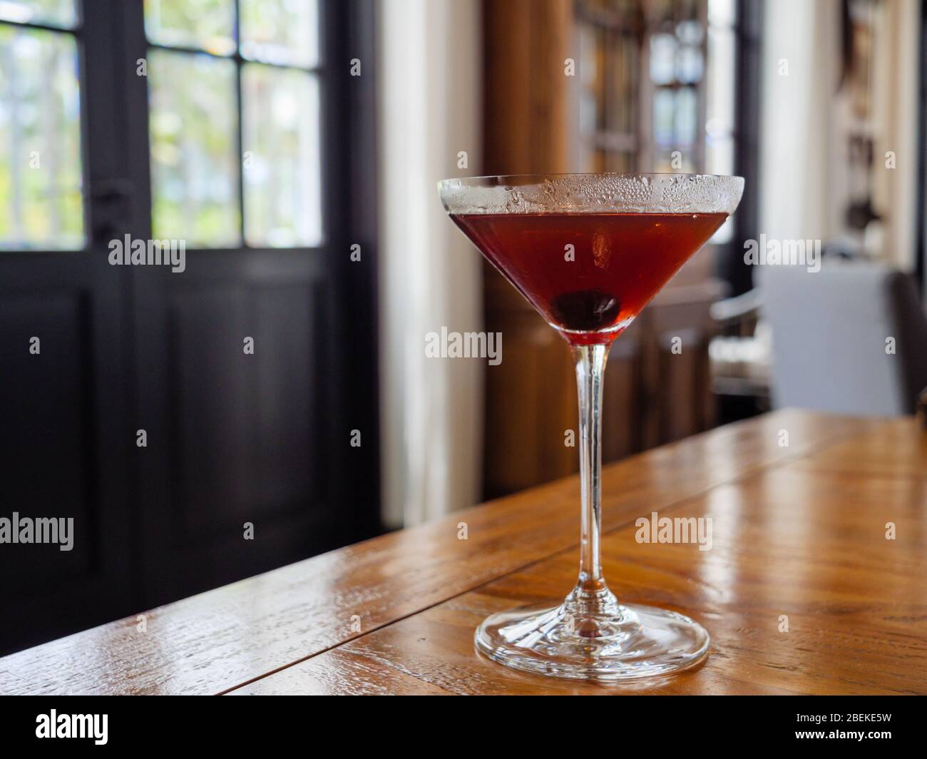 Red-brown cocktail with an olive in a martini glass during daytime in home / restaurant setting with copy space Stock Photo