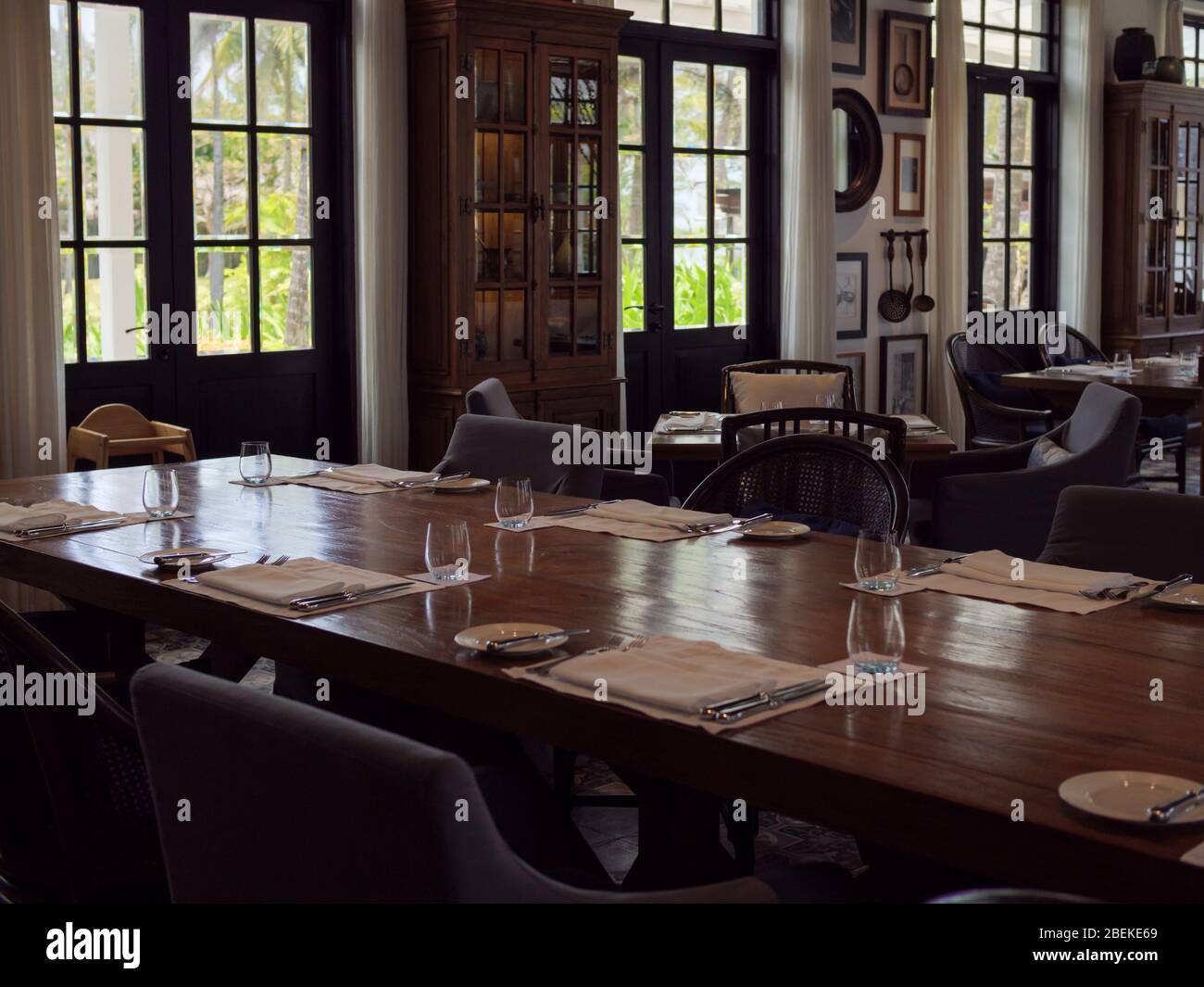 BINTAN, INDONESIA – 7 MAR 2020 – Set table in the interior of an empty Western / European style restaurant in a beach holiday resort with dark wood fu Stock Photo