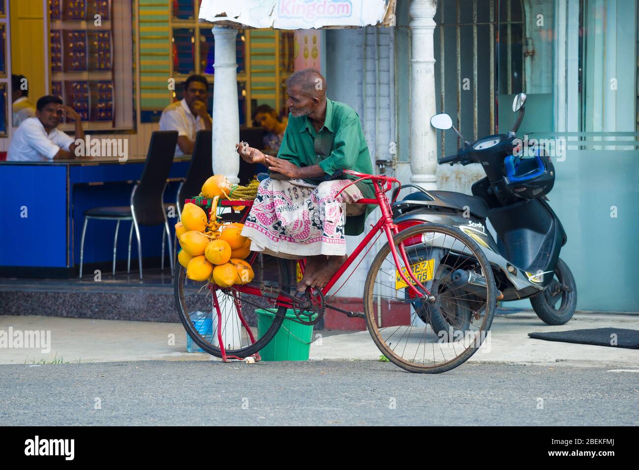 AMBALANGODA, SRI LANKA - FEBRUARY 19, 2020: Elderly Sri Lankan man sells ripe coconuts on city street Stock Photo