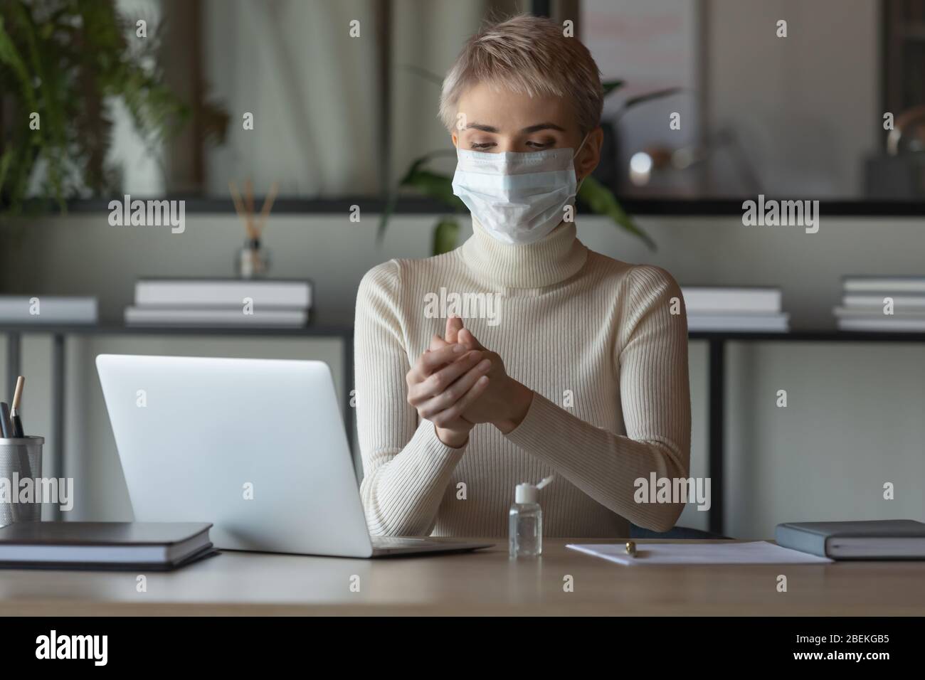 Female employee cleanse hands with sanitizer at workplace Stock Photo