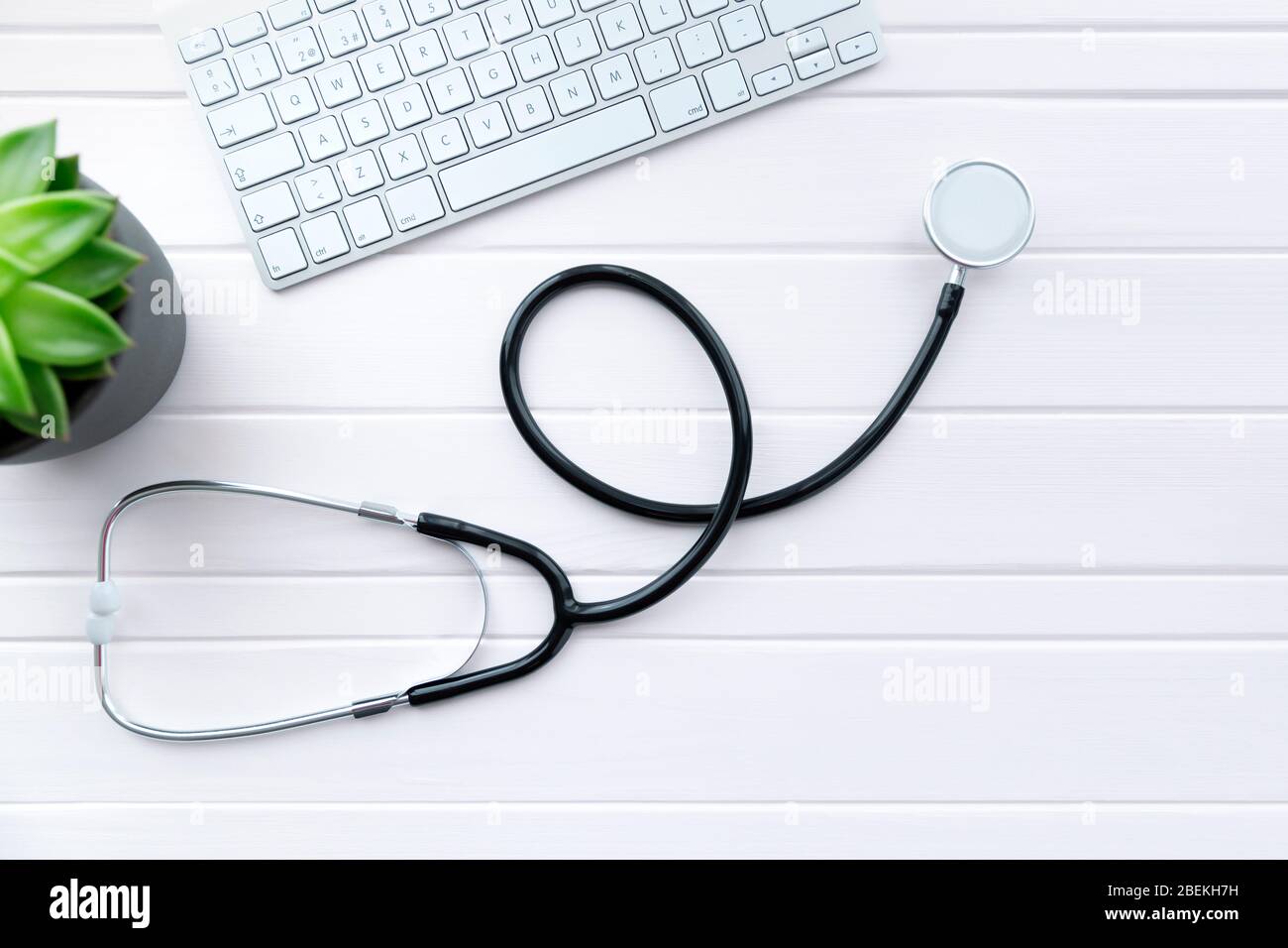 Stethoscope on white wooden table next to computer keyboard and plant ...