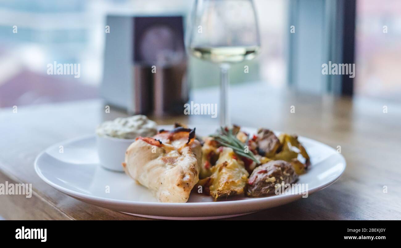 Restaurant meal, meat, potatoes and sauce. Glass of white wine on wooden table Stock Photo