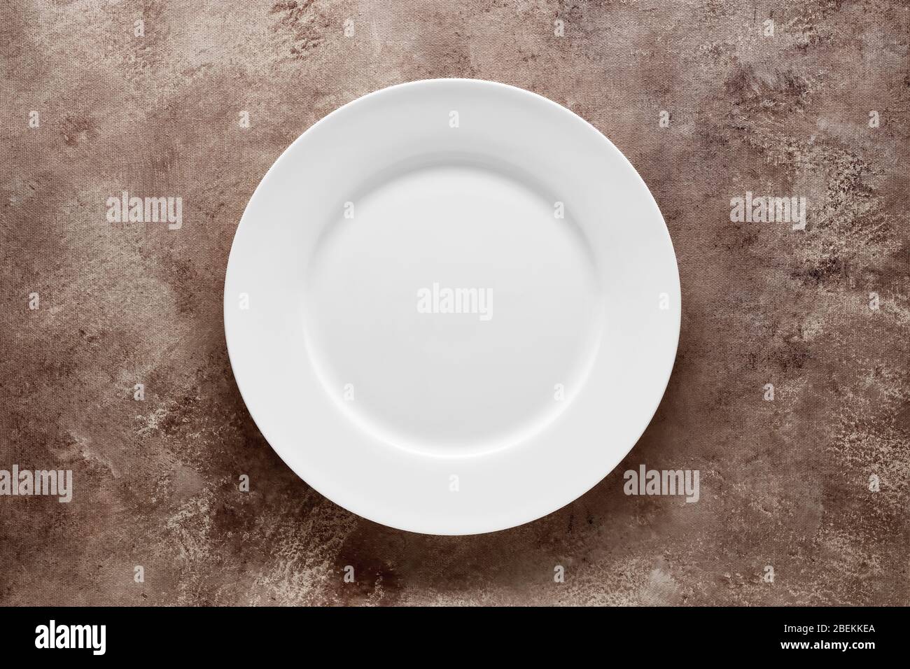 Empty white plate on brown textured background with copy space. Top view. Stock Photo