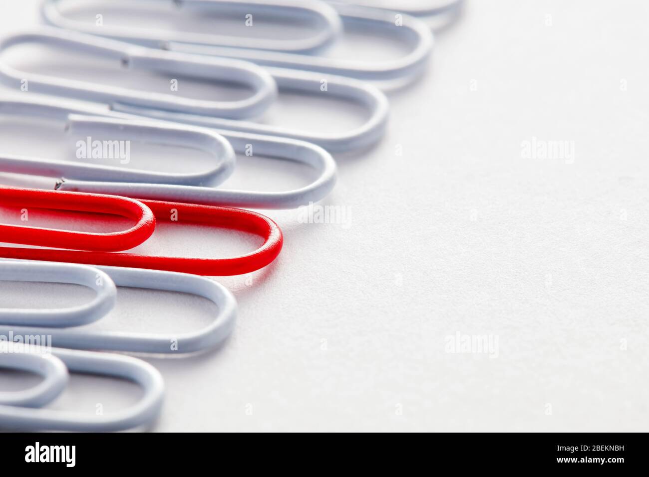 Red paper clip stands out from the crowd among white paper clips. Stock Photo