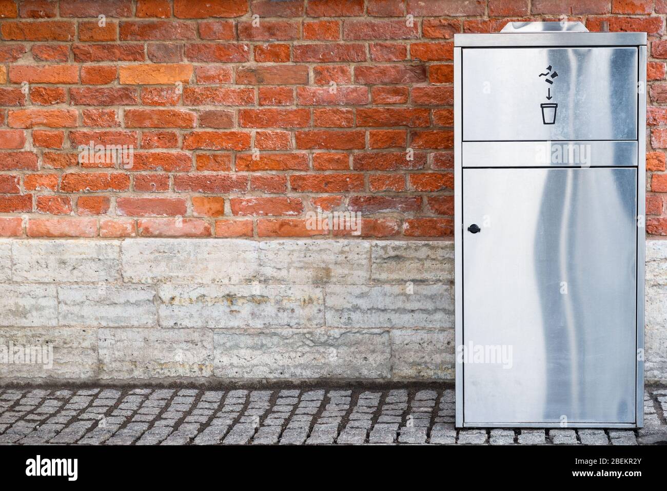 Modern stainless steel/metal trash can for recycling plastic and paper cups over brick wall outdoors. Free space. Stock Photo