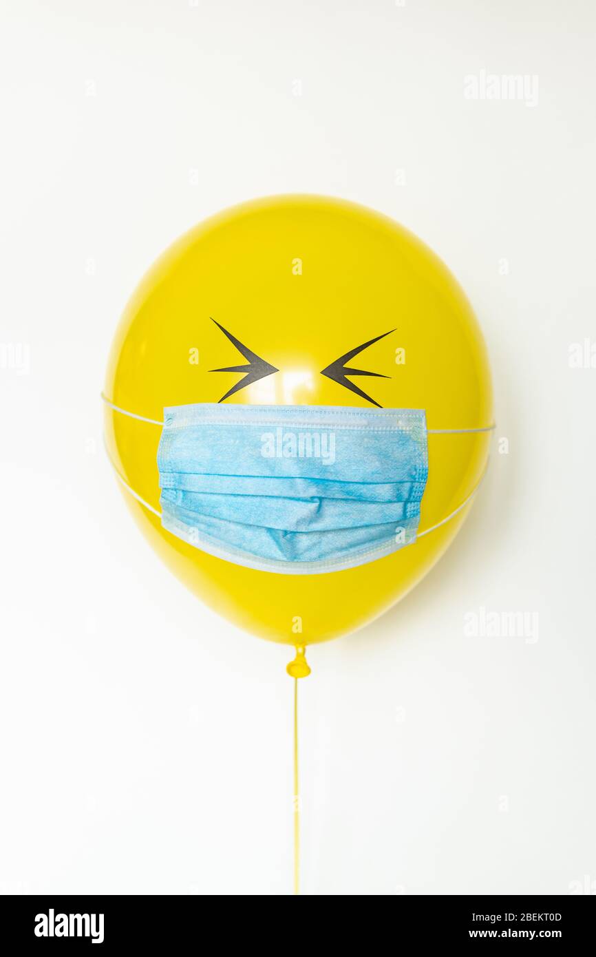 Yellow balloon with a medical mask and doodle closed eyes. Conceptual image of Birthday party during Corona virus quarantine lockdown Stock Photo