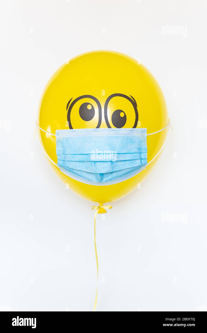 Yellow balloon with a medical mask and doodle shocked eyes. Conceptual image of Birthday party during Corona virus quarantine lockdown Stock Photo