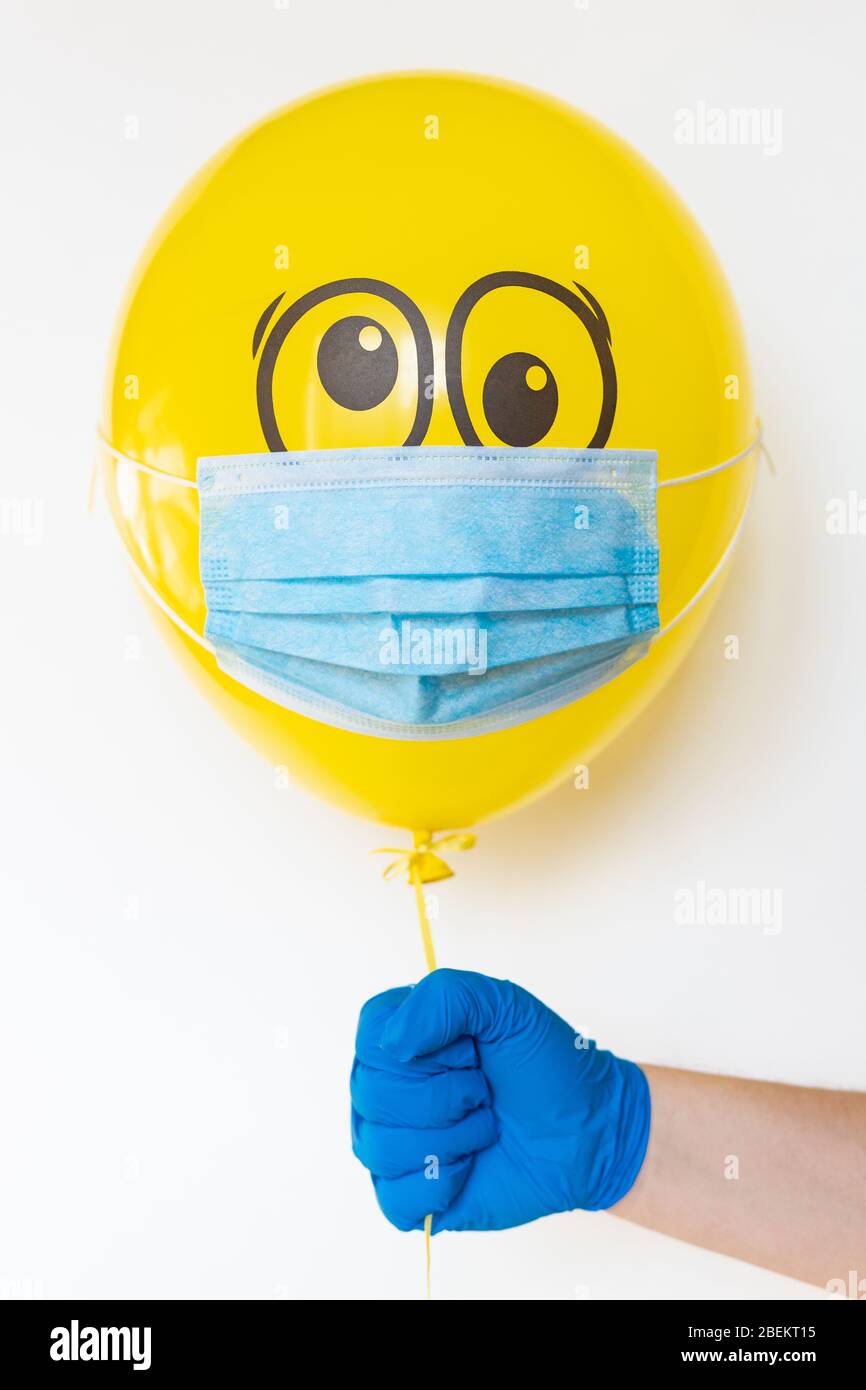 Hand in a rubber glove holding a yellow balloon with a medical mask and