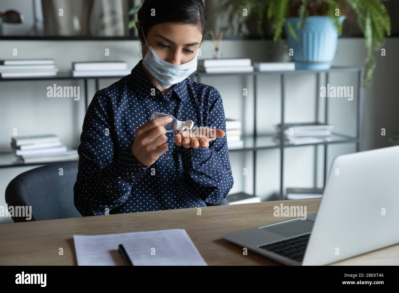 Young Indian woman in face mask cleanse hands with sanitizer Stock Photo