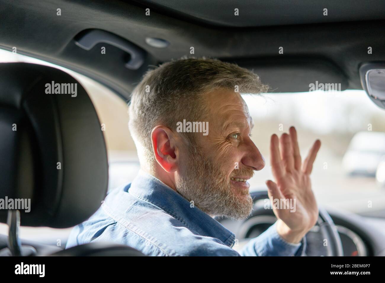 Profile of a friendly car driver with graying hair and beard greeting someone with his hand Stock Photo