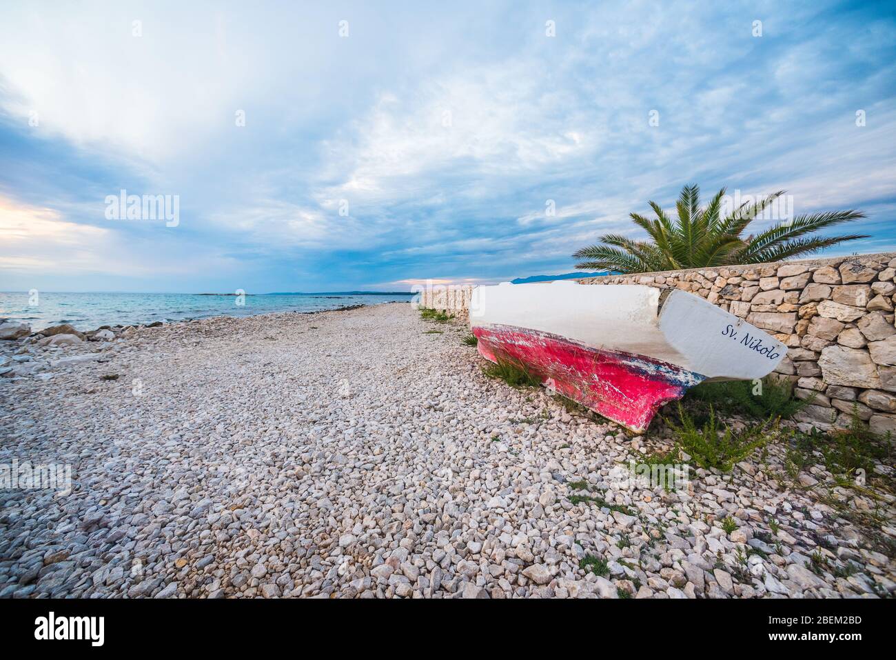 sunset on croatian stony beach with boat Stock Photo