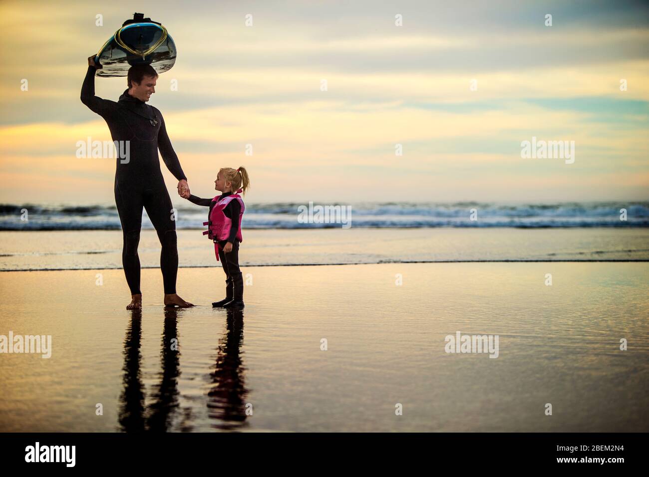 Surfer holding hands with his young daughter at the beach Stock Photo