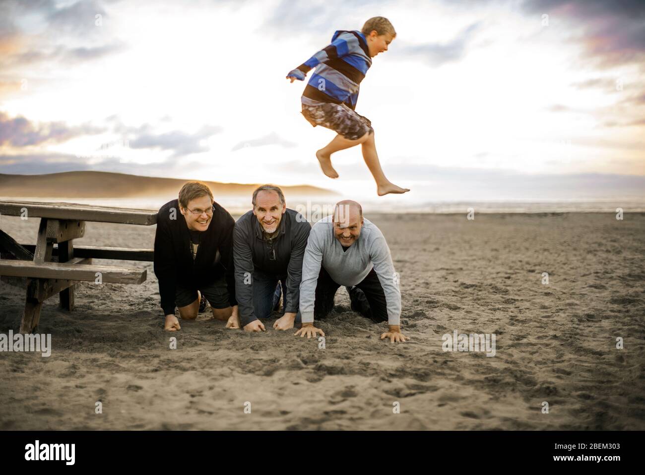 Playful young boy leaping over three kneeling men Stock Photo