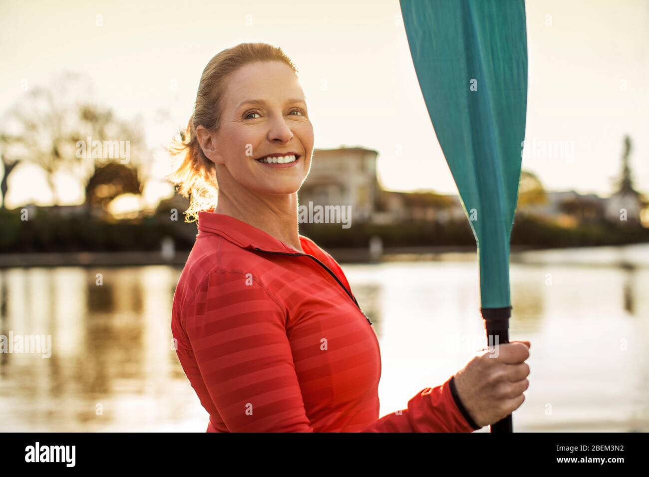 Portrait of a happy mid adult woman holding an oar by a lake Stock Photo