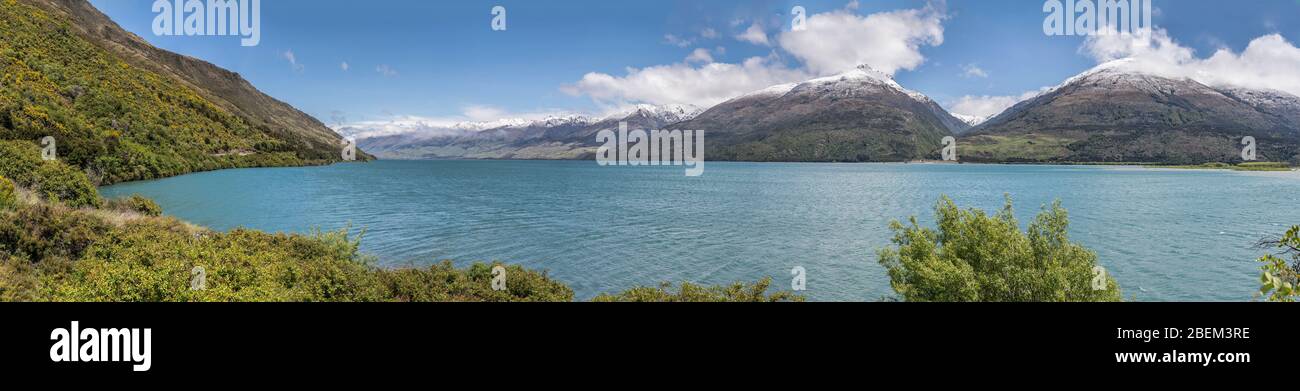 landscape of Wanaka Alpine lake with green shores and snow capped mountains, shot in bright spring light from Boundary creek beach, Otago, South Islan Stock Photo
