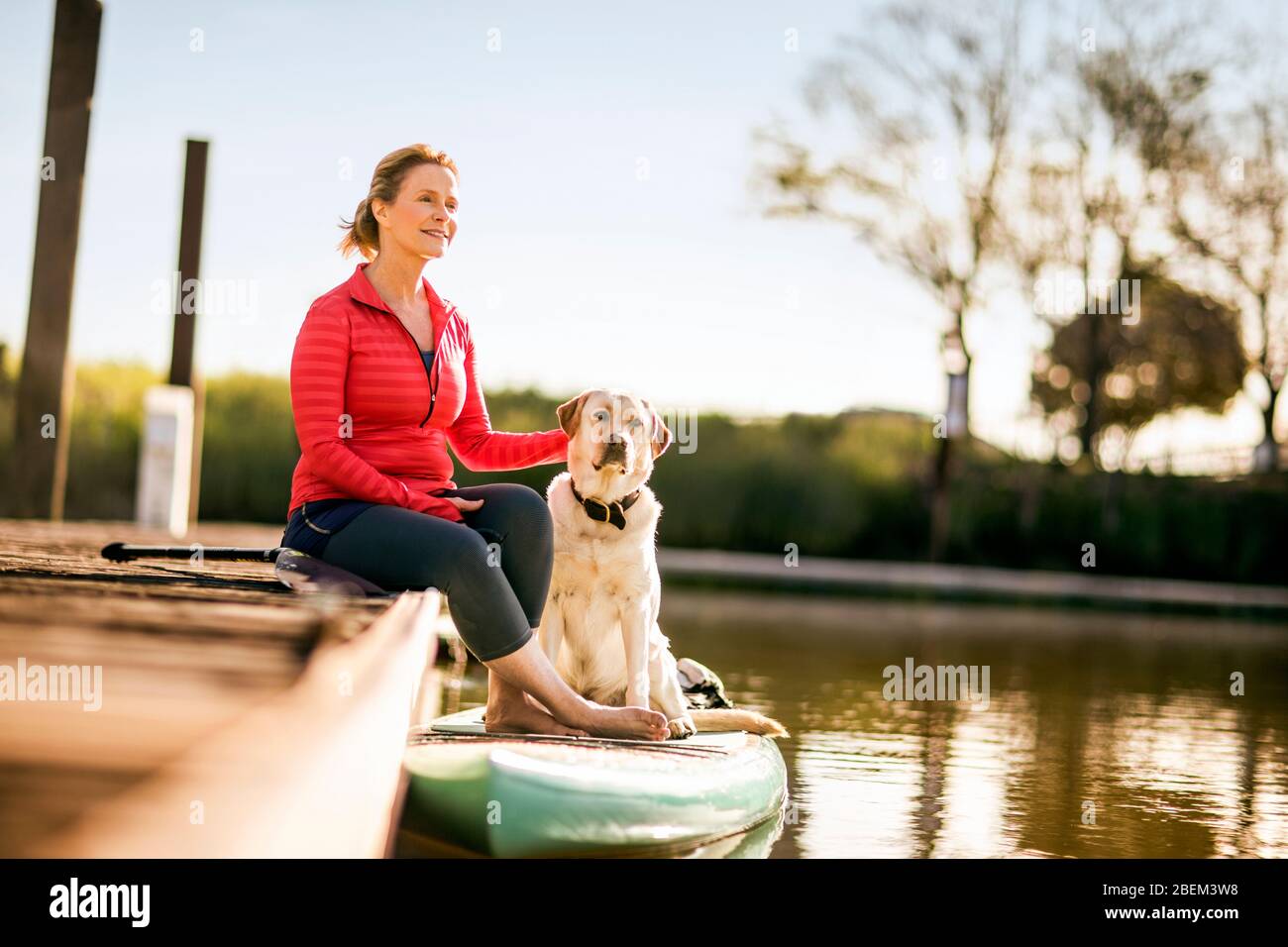 Mid adult woman sitting on a dock with her pet dog Stock Photo