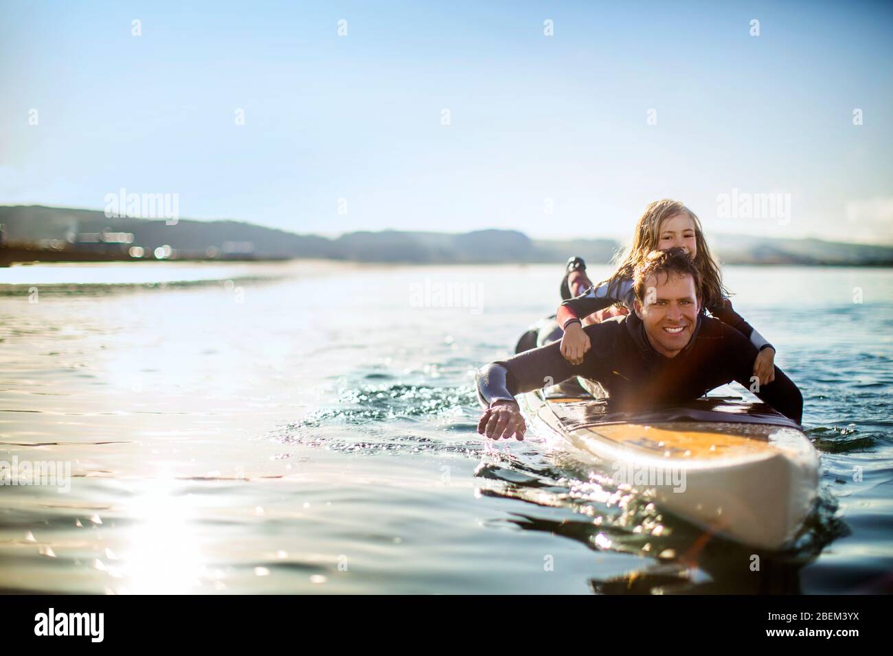 Smiling mid adult man paddle boarding with his young daughter Stock Photo