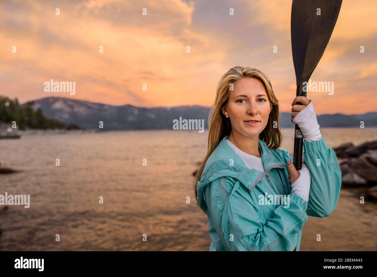Mid adult woman standing by a lake at sunset holding a paddle Stock Photo
