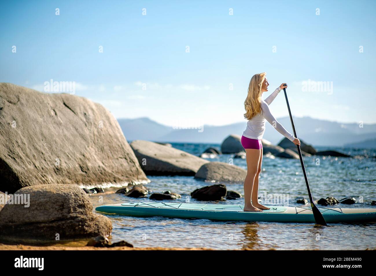 Active young woman paddle boarding across a lake Stock Photo