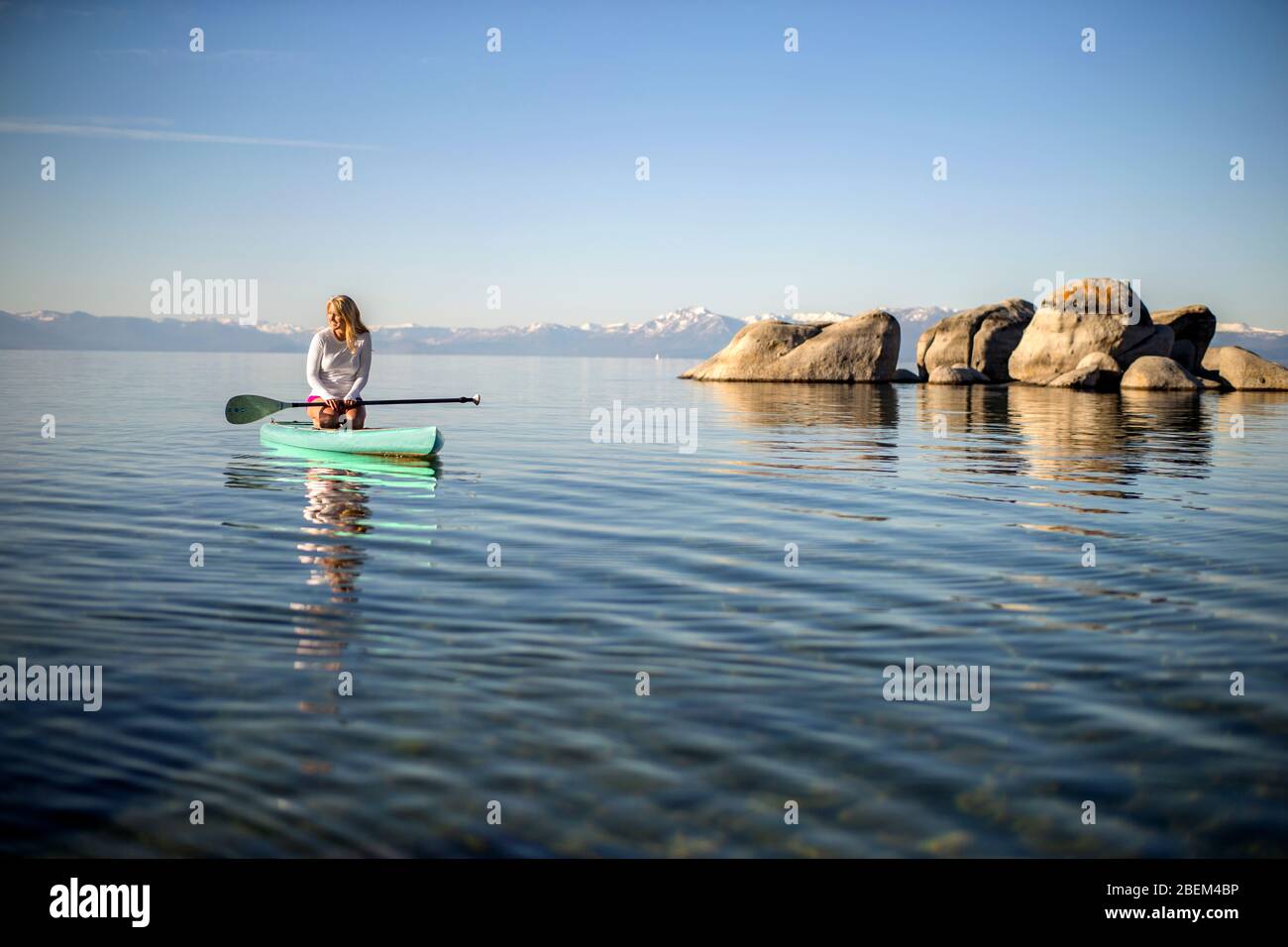 Young woman paddle boarding across a lake Stock Photo