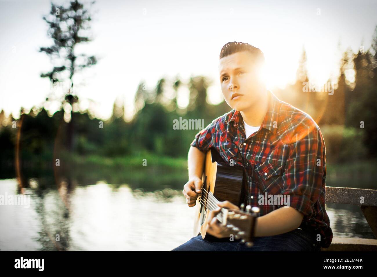 Young man playing guitar by a lake Stock Photo