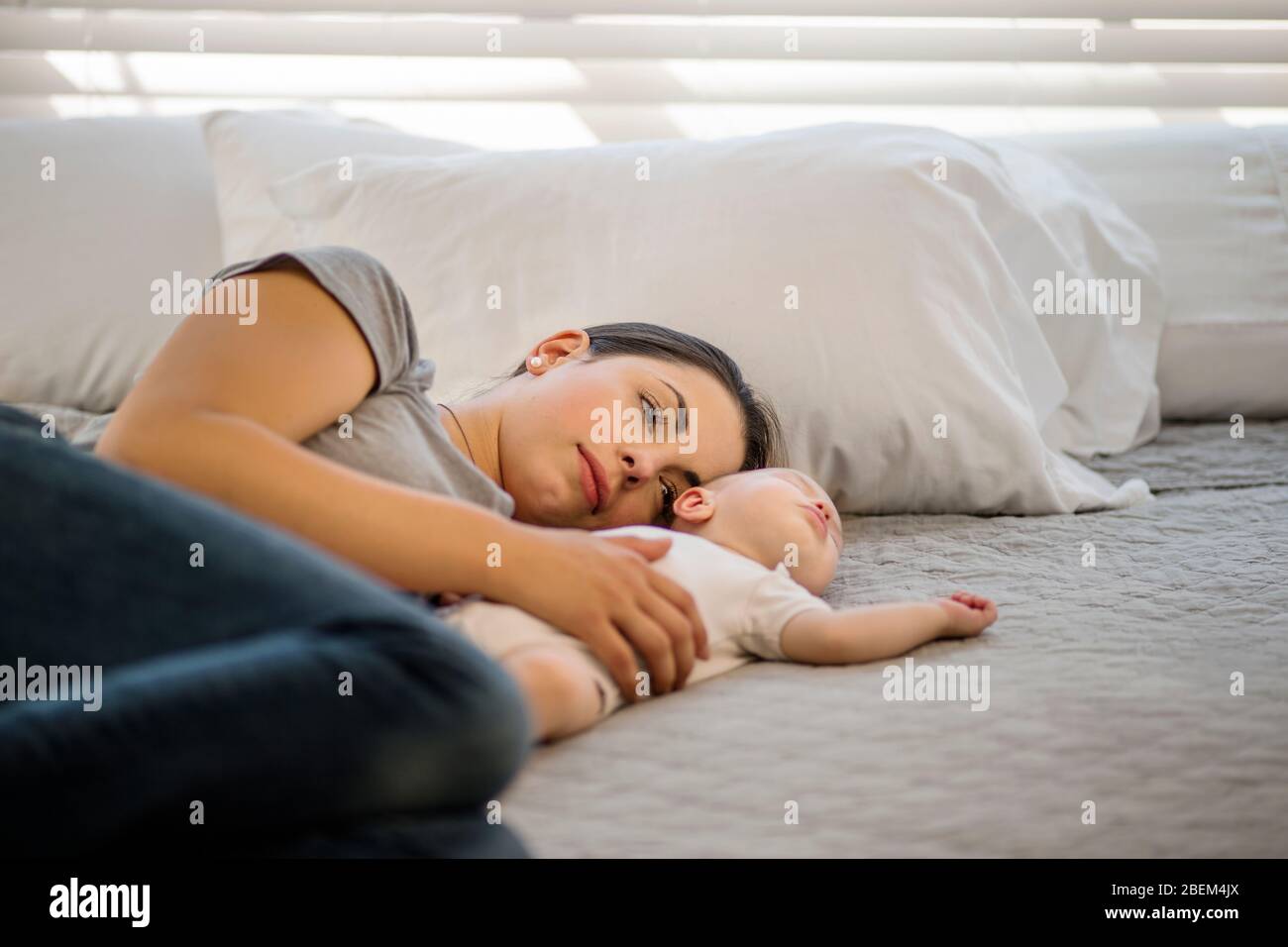 Mid adult mother lying down on a bed with her sleeping baby Stock Photo