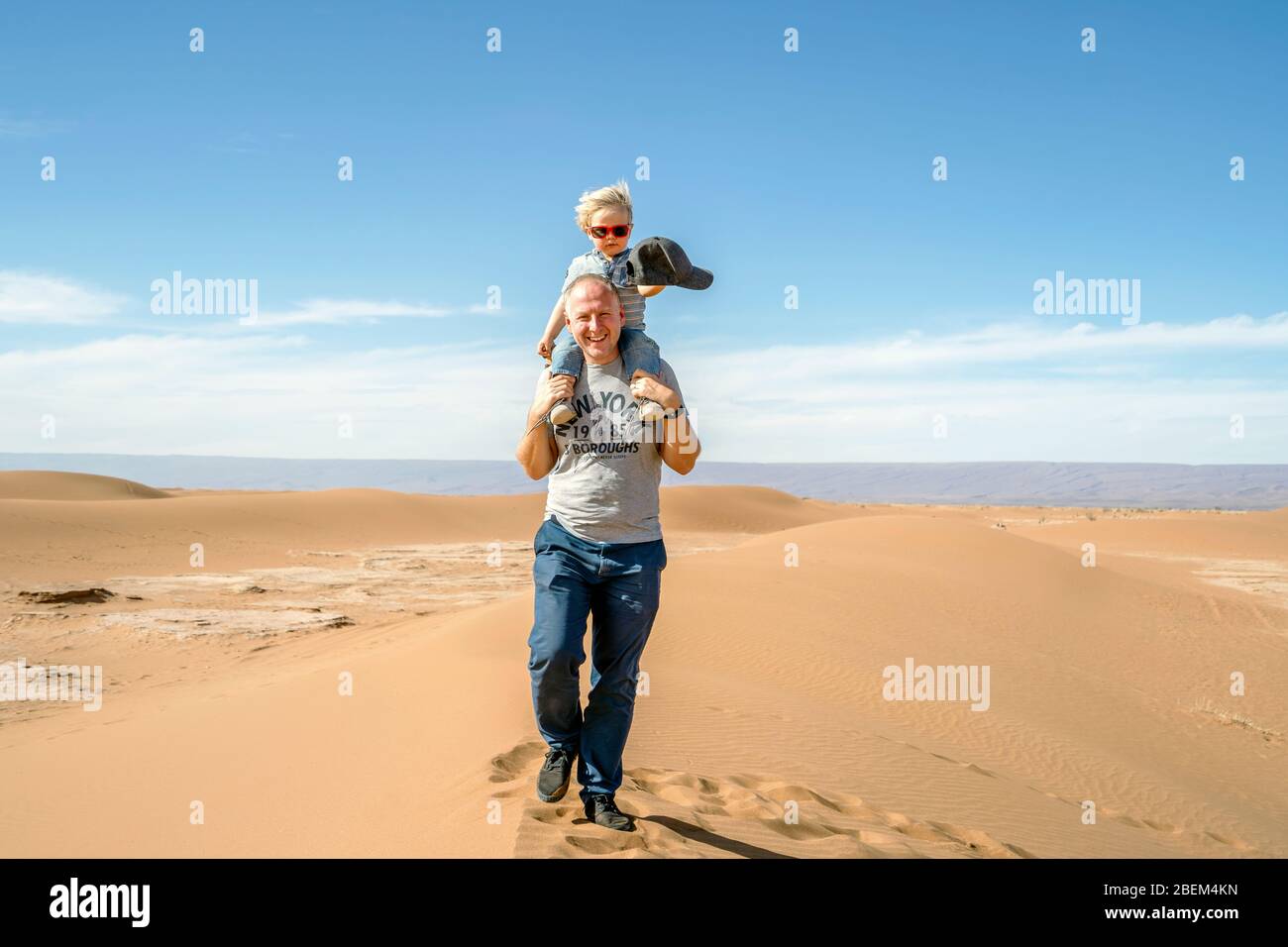 Father walking with piggybacked 2 years old son through Sahara Desert in Morocco, Africa Stock Photo